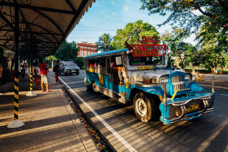 Manila, Philippines - November 10, 2018: Ordinary people wait for transport at a bus stop while blue Jeepney passes by on November 10, 2018, in Manila, Philippines.のeditorial素材