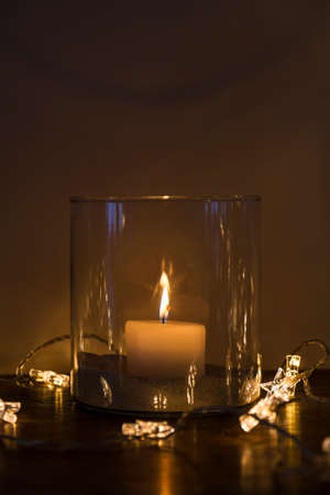 Burning candle and star-shaped lights on a wooden tableの写真素材
