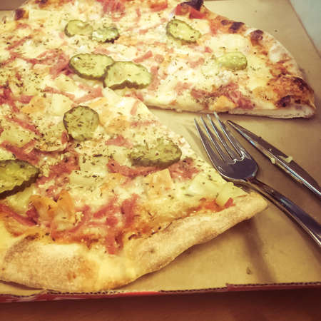 Takeaway pizza with on slice taken and fork and knife in cardboard boxの写真素材