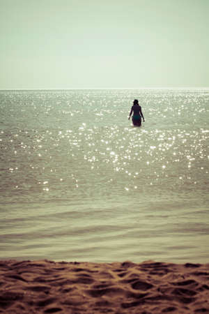 Sunny sandy beach with a woman in water