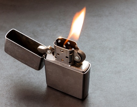 Silver metal lighter on dark background with flame.の写真素材