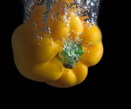 Yellow paprika splash in water on black background. の写真素材
