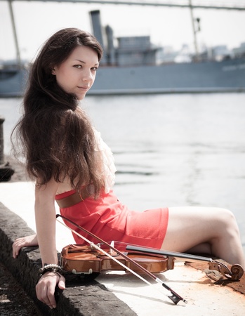Pretty young female with violin sitting on a pier.の写真素材