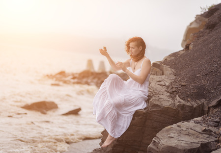   Portrait of redhead woman holding zen stones in hand with sea in foggy day  Soft focus  With sunshine effect の写真素材