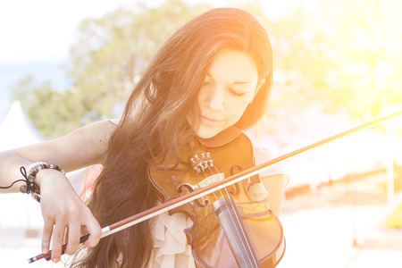 Portrait of a young female playing the violin. With sunshine. Color toned image.の写真素材