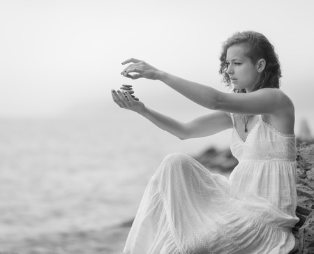 Portrait of a woman holding zen stones in hand with sea background in foggy day. Black and white.の写真素材