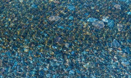 Sea bottom with pebbles through clear water. Winter. Blue toned.