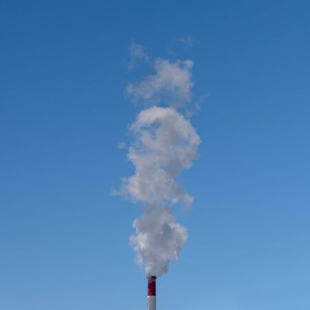 Industrial pipe with smoke on a blue sky background.