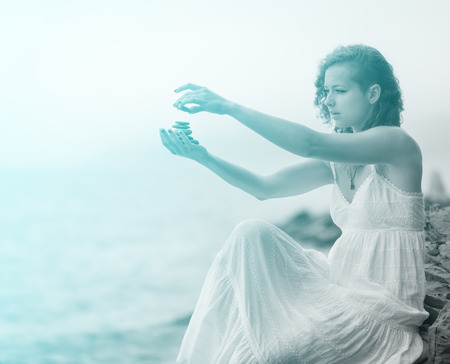 Portrait of redhead woman holding zen stones in hand with sea background in foggy day. Soft focus. With blue light effect.の写真素材