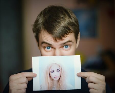 Young man holding in hand photo of a beautiful girl.の写真素材