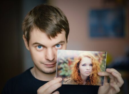 Young man holding in hand photo of a beautiful girl.
