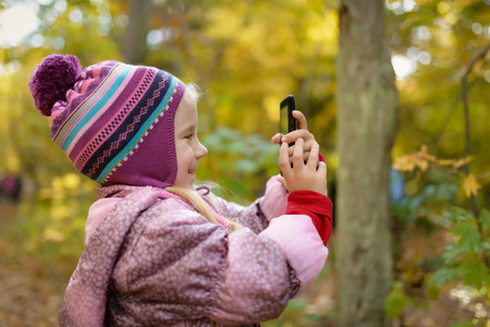 Little girl making photo or video with smartphone in the forest. Selective focus with shallow depth...