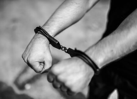 A mens hands in handcuffs. Selective focus with shallow depth of field. Black and white toning.の写真素材