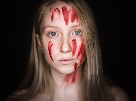 Portrait of young woman with paint on her face on dark background.の写真素材