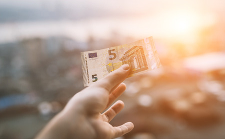 Five euro in hand over city background at sunset.の写真素材