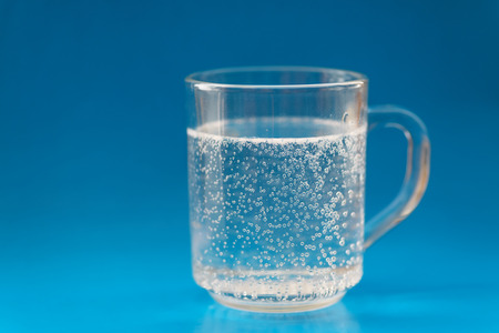 Glass cup with bubbles of air on blue background. Selective focus wtih shallow depth of field.の写真素材