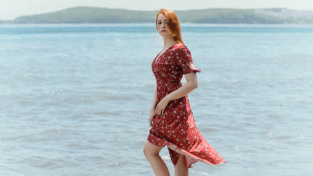 Redhead woman in dress enjoys a walking near the sea shore.の写真素材