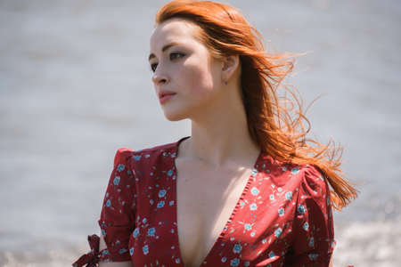 Redhead woman in dress enjoys a walking near the sea shore.の写真素材