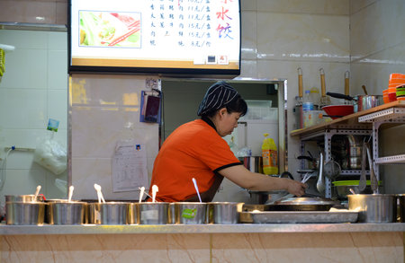 MISHAN, CHINA - JULY 28, 2019: Asian elderly woman cooking food on the kitchen in a fast food cafe.のeditorial素材