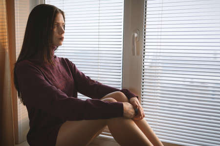 Sad woman looking through the window.の写真素材