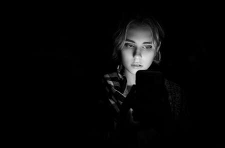 Young woman using smartphone on the street by night. Black and white toned.の写真素材