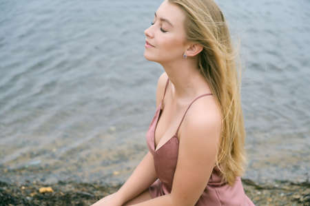 Young woman in pink dress sitting on sand and enjoys sea.の写真素材