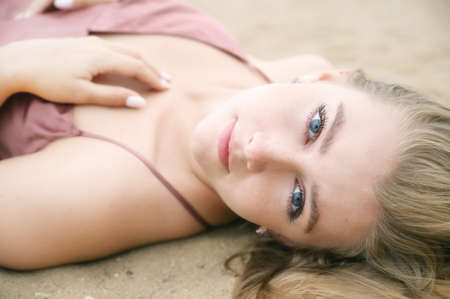 Young woman in pink dress lying on the sand and enjoys sea.の写真素材