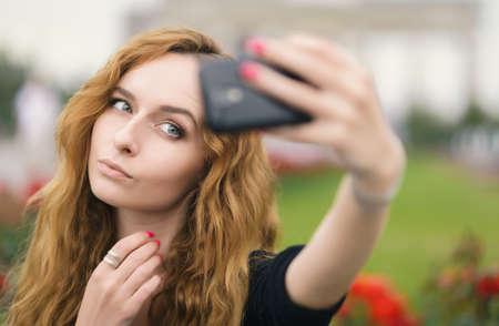 Young redhead girl taking a selfie outdoors on sunny day.の写真素材