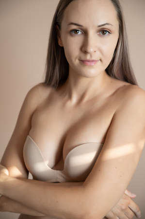 Beautiful adult woman in bra posing against beige wall.の写真素材