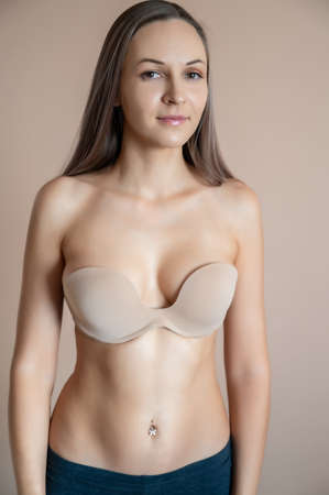 Beautiful adult woman in bra posing against beige wall.の写真素材