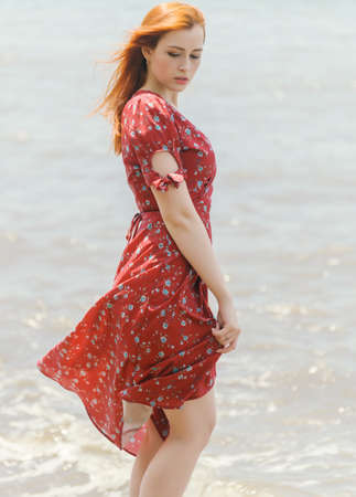 Redhead woman in dress enjoys a walking near the sea shore.の写真素材