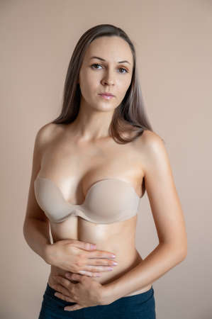 Beautiful adult woman in bra posing against beige wall.の写真素材