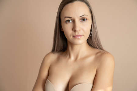 Beautiful adult woman in bra posing against beige wall.の写真素材
