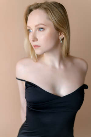 Graceful young woman in a black top posing against beige wall.の写真素材