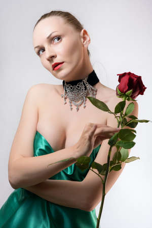 Woman in green dress one red rose in hand on light background.の写真素材