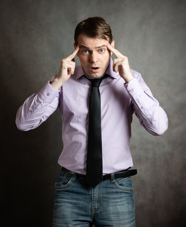 Portrait of pensive young man in pink shirt and dark tie, against dark background.の写真素材