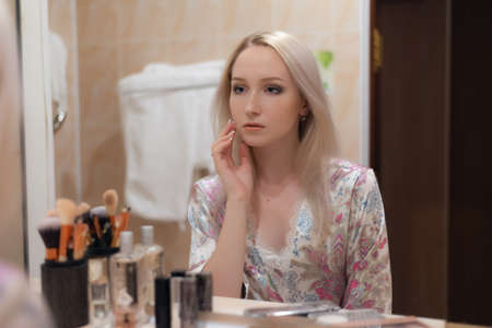 Young woman looking in mirror while applying makeup. Selective soft focus.の写真素材