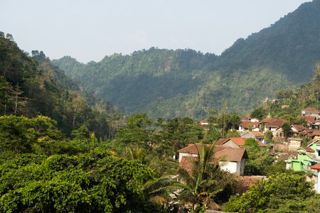 Small village homes are nestled at the base of a lush tropical mountain valley in the daylight.の写真素材