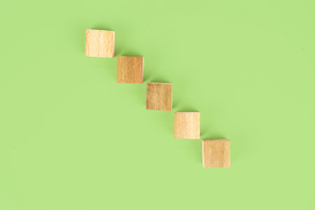 A minimalist composition featuring wooden blocks arranged in a descending diagonal line against a solid green backdrop, creating a simple yet visually engaging pattern.の写真素材