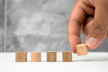 A hand carefully places a wooden block in a row, symbolizing order, planning, and decision-making on a clean white surface.の写真素材