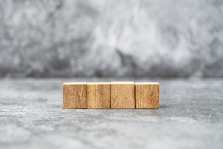 A row of four blank wooden blocks sits on a textured gray surface, perfect for displaying letters, numbers, or symbols in creative projects.の写真素材