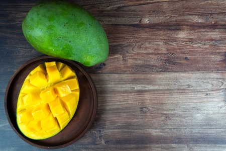 Single whole green mango rests beside a cubed yellow half on a dark rustic wood background.の写真素材