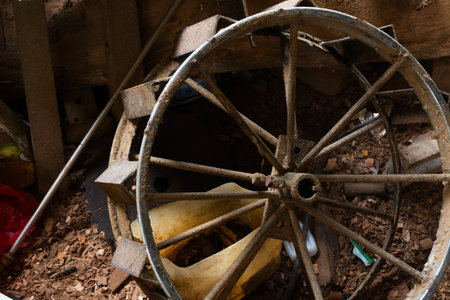Dirty, rusty spoked metal wheel and machinery parts in dark workshop.の写真素材