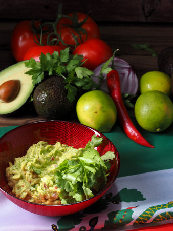 Guacamole in a red bowl, with ingredients at the back. All displayed over a background.の写真素材