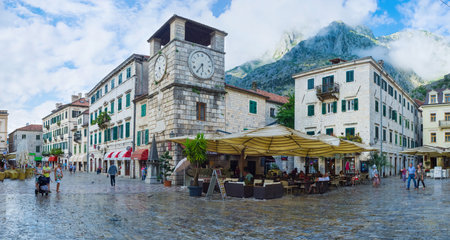 KOTOR, MONTENEGRO - JULY 12, 2014: The Main Square boasts many street cafes, tiny shops, scenic Kampana tower and the view on the foggy mountains on the background, on July 12 in Kotor.のeditorial素材