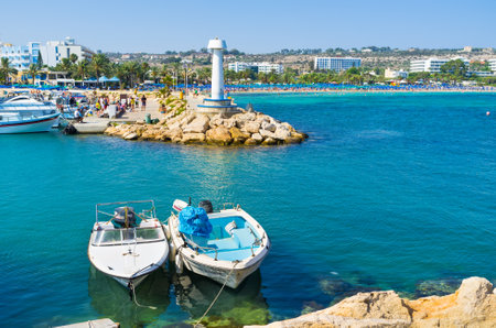 The port of Ayia Napa with the couple of moored boats and the view on the busy beaches on the background, Cyprus.のeditorial素材