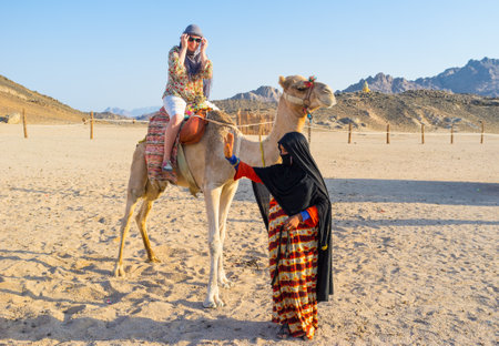 HURGHADA, EGYPT - OCTOBER 5, 2014: The tourist feels happy during the camel ride and the young girl-cameleer waves her hand to the friends, on October 5 in Hurghada.のeditorial素材
