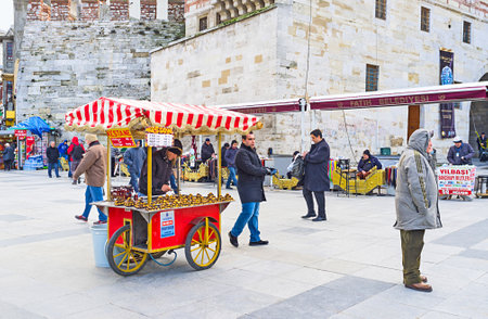 ISTANBUL, TURKEY - JANUARY 13, 2015: The  roasted chestnut cart on Rustem Pasha Square with the shoeshiners on the background, on January 13 in Istanbul.のeditorial素材