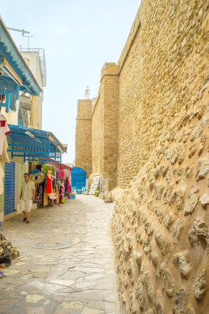 HAMMAMET, TUNISIA - SEPTEMBER 6, 2015: The shopping street borthers with the old fortress wall, surrounding Medina, on September 6 in Hammamet.のeditorial素材