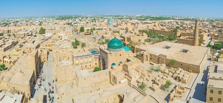 The yellow roofs of Khiva with the bright green dome of Pahlavon Mahmud Mausoleum and Kalta Minor Minaret on the background, Uzbekistan.の写真素材